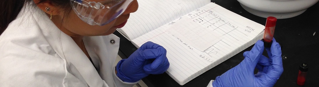 student in lab coat and gloves holds vial