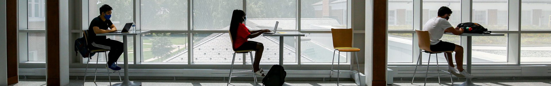 three students sit at desks in front of window